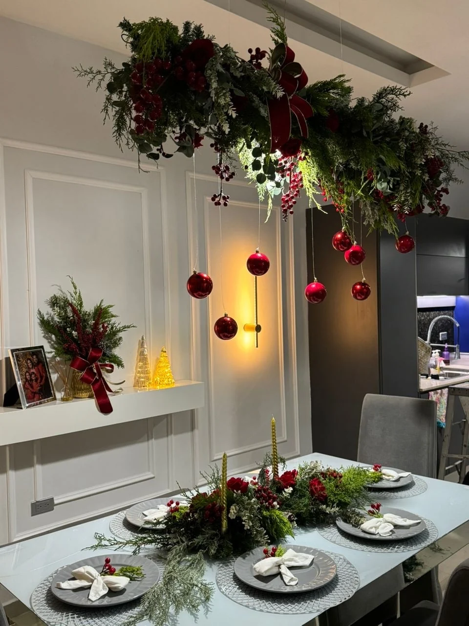 Christmas dining table beneath a suspended evergreen garland with red baubles and burgundy ribbon.