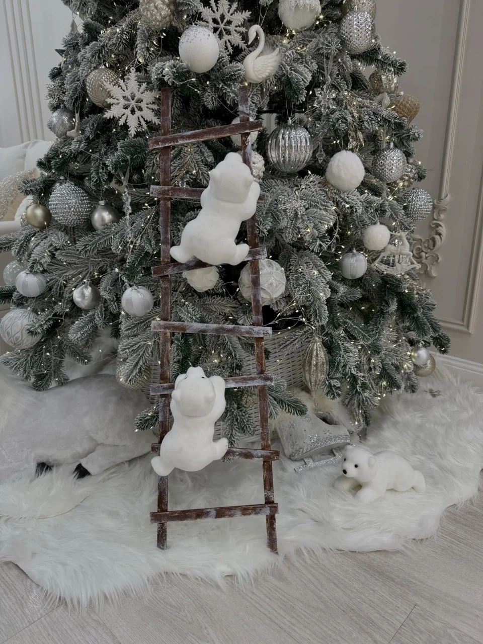 Small white polar bear decorations climbing a wooden ladder beside silver baubles, swan ornaments and a white tree skirt.