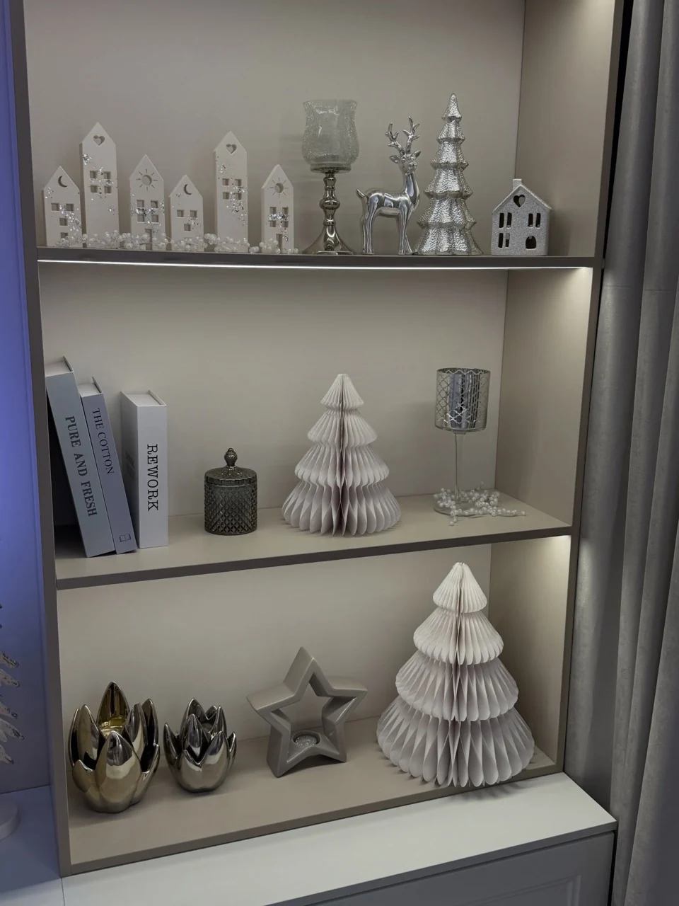 White honeycomb paper trees, miniature houses, a silver reindeer and candle holders on illuminated shelves.