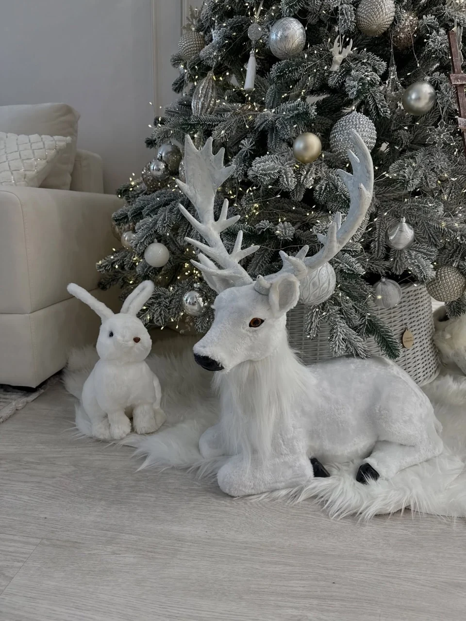 White reindeer and rabbit decorations on a faux-fur tree skirt beneath silver and white Christmas ornaments.