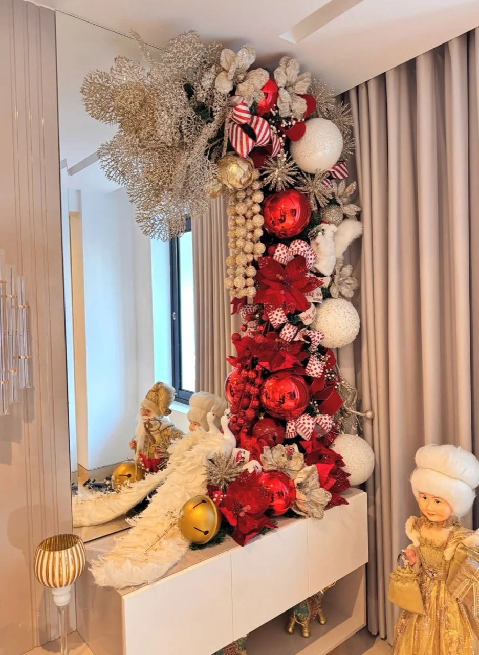 Tall mirror framed with red and white baubles, striped ribbon and gold foliage beside festive figures and bell decorations.